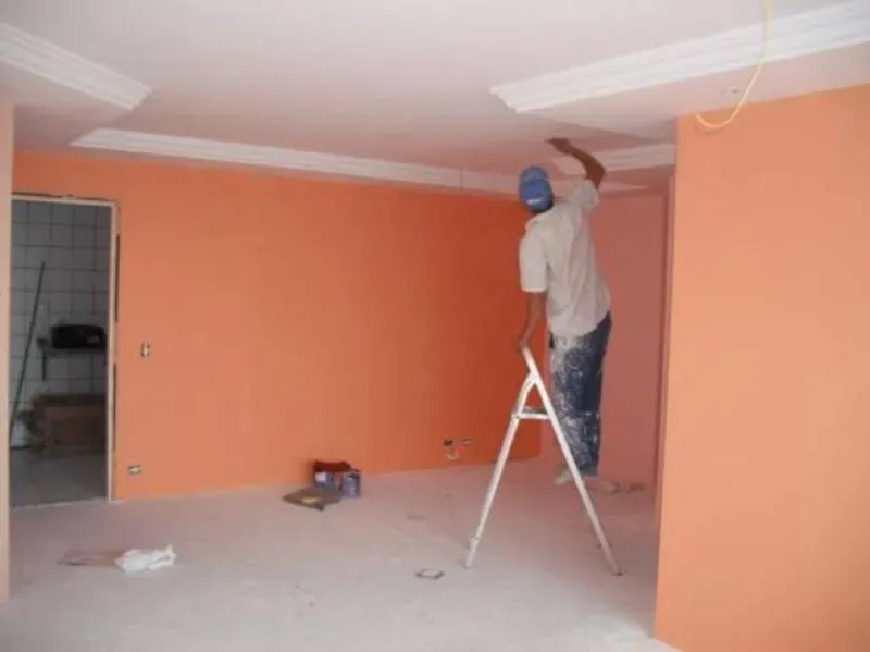 Sala sendo pintada em laranja com gesso branco no teto
